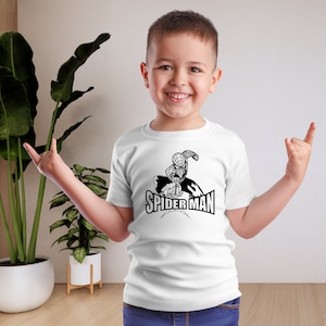 Peut inclure: Un t-shirt blanc avec un motif noir et blanc de Spider-Man et le texte "SPIDER-MAN". Le t-shirt est porté par un enfant souriant. Le t-shirt est un vêtement pour enfants.