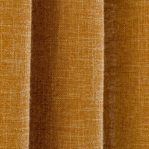 May include: Close-up of textured, mustard-coloured fabric, possibly a curtain or upholstery material. The fabric has a woven appearance with vertical folds, creating shadows and depth. The colour is a warm, earthy tone.