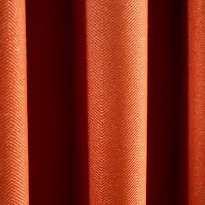 May include: Close-up of a textured orange fabric with a herringbone pattern. The fabric is folded in a way that creates a series of vertical lines.