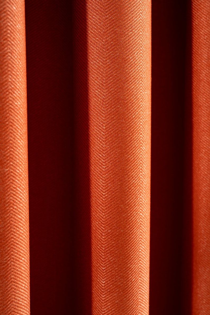 May include: Close-up of a textured orange fabric with a herringbone pattern. The fabric is folded in a way that creates a series of vertical lines.