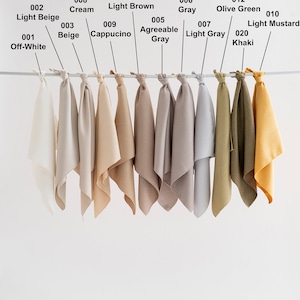 May include: Ten fabric swatches hanging from a rod, showcasing a range of colors from off-white to mustard yellow. The swatches are labeled with numbers and color names.