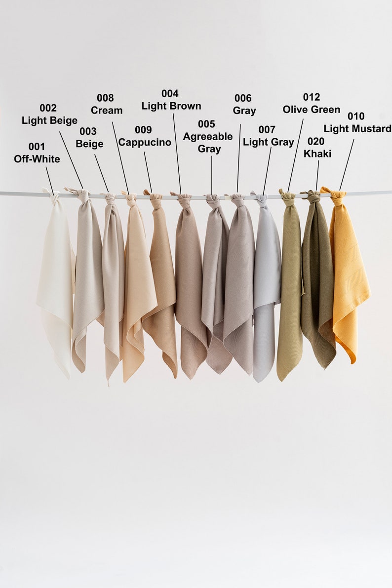 May include: Ten fabric swatches hanging from a rod, showcasing a range of colors from off-white to mustard yellow. The swatches are labeled with numbers and color names.