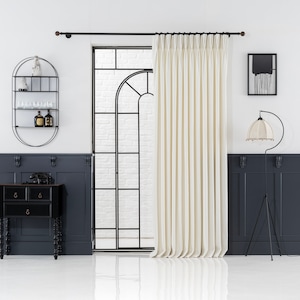 May include: A white curtain with pleats hangs in front of a black metal framed window. A black metal shelf with glass shelves is on the left wall. A black metal floor lamp with a white lampshade is on the right side of the image.