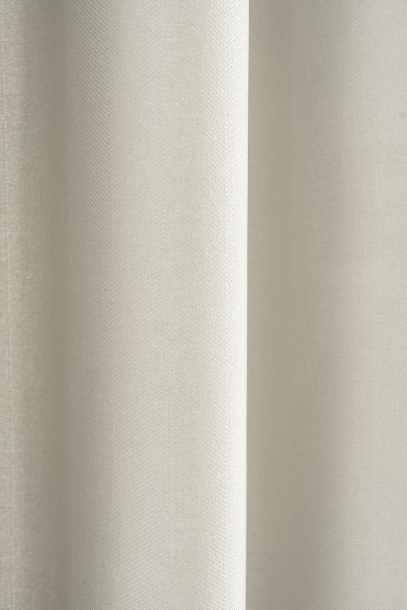 May include: Close-up of a white curtain with a subtle herringbone pattern. The fabric has a smooth, slightly textured surface.