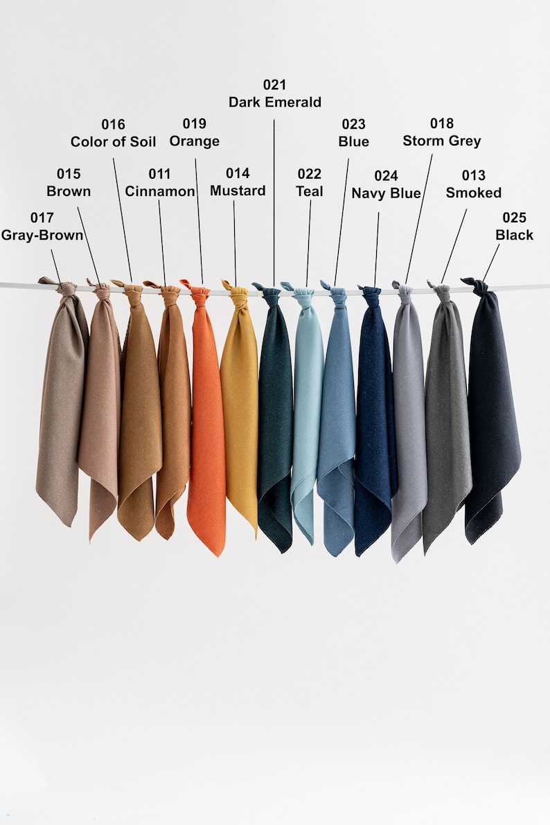 May include: A row of 12 fabric swatches hanging from a string. The swatches are in various colors, including brown, orange, mustard yellow, teal, blue, navy blue, gray, and black. The swatches are labeled with numbers and names, such as "Color of Soil", "Cinnamon", "Mustard", "Teal", "Navy Blue", "Smoked", and "Black".