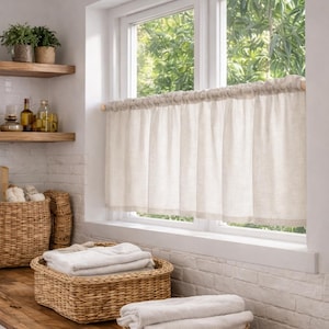 Könnte beinhalten: Helles Badezimmer mit einem Fenster mit cremefarbenem Vorhang. Weidenkörbe mit gefalteten weißen Handtüchern. Holzregale mit Pflanzen und Flaschen. Der Raum hat eine rustikale, spa-ähnliche Ästhetik.