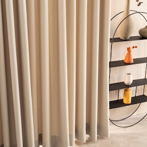 May include: A set of beige curtains with a subtle texture, hanging in a room with a black metal shelf unit holding decorative vases. The shelf unit is in the shape of a half circle.