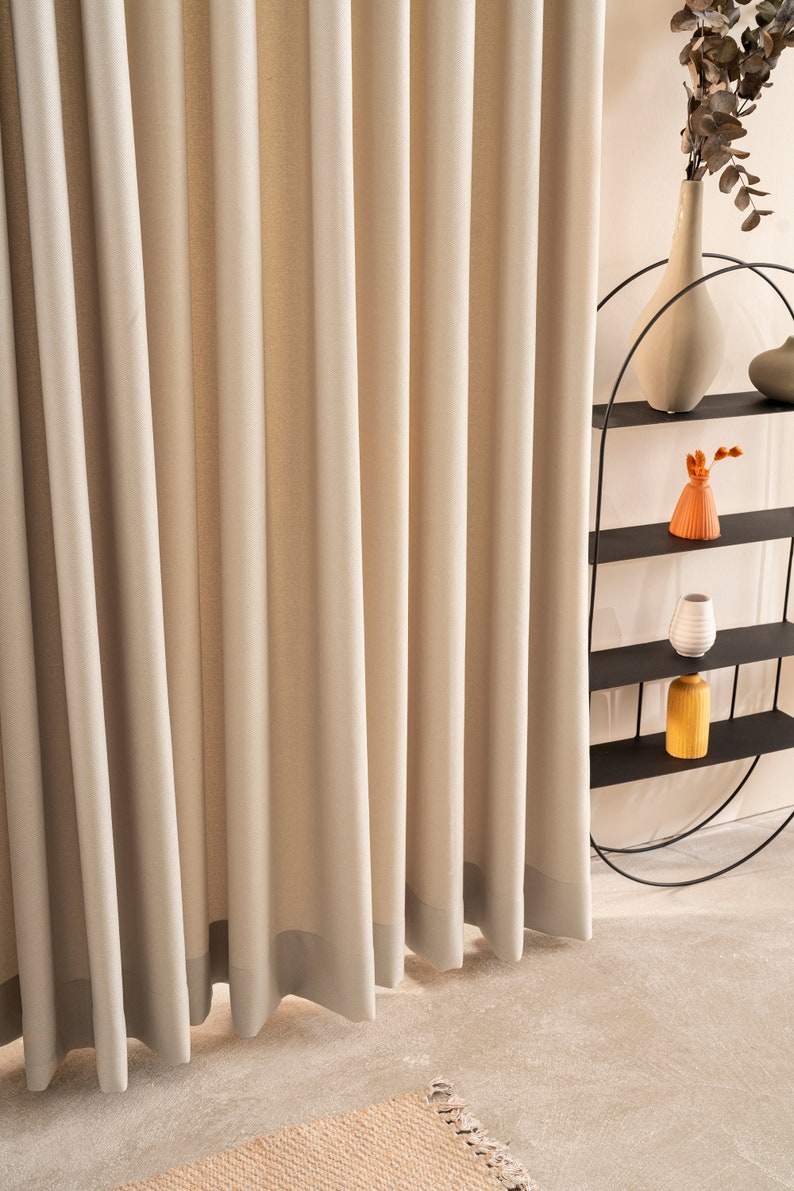 May include: A set of beige curtains with a subtle texture, hanging in a room with a black metal shelf unit holding decorative vases. The shelf unit is in the shape of a half circle.