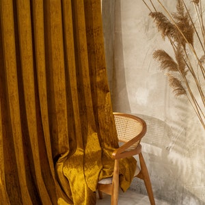 Peut inclure: Un rideau en velours jaune moutarde drapé sur une chaise en bois avec un siège en rotin tissé. La chaise est dans une pièce avec un mur beige clair et de l'herbe de pampa séchée.