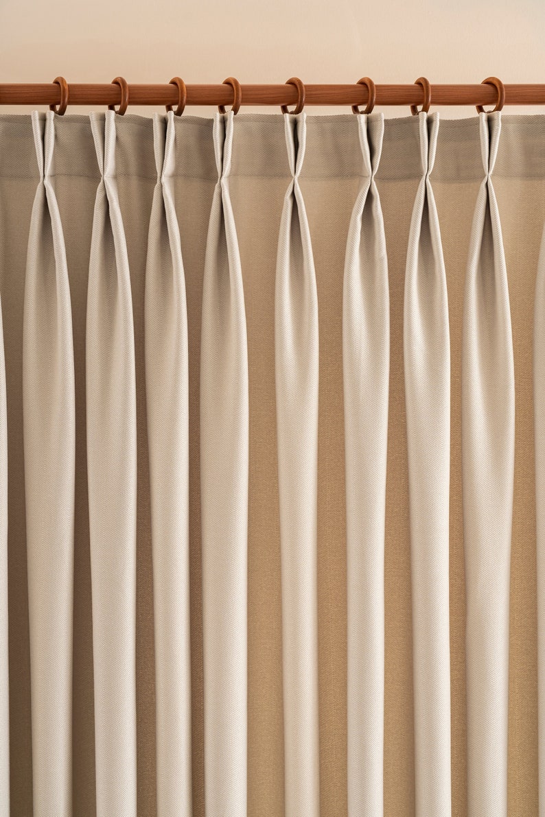 May include: White curtains with pleats hanging from a wooden curtain rod.