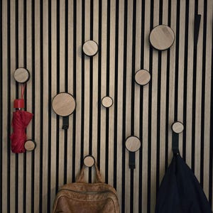May include: A wooden wall with black vertical slats and round wooden hooks. There are several hooks with items hanging on them, including a red umbrella, a brown leather backpack, and a black jacket.