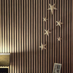 Op de afbeelding: Een decoratieve muur met verticale houten latten in afwisselende lichte en donkere tinten. Verschillende witte papieren sterornamenten zijn aan de muur bevestigd. Een ingelijste foto en een lamp staan op een wit oppervlak.
