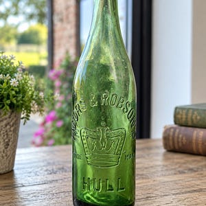 May include: A vintage green glass bottle featuring embossed text that reads Mayors & Robson's, a central crown graphic, and the word Hull at the base. The bottle has a narrow neck, a rounded rim, and a cylindrical body with a smooth, translucent finish.