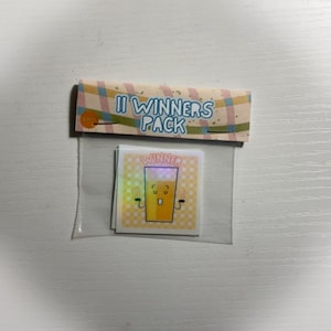 Puede incluir: Una bolsa de plástico transparente con un encabezado a rayas amarillo y azul que dice "11 Winners Pack". Dentro de la bolsa hay una pegatina con un vaso de jugo de naranja de dibujos animados con una cara sonriente y la palabra "Winner" encima.