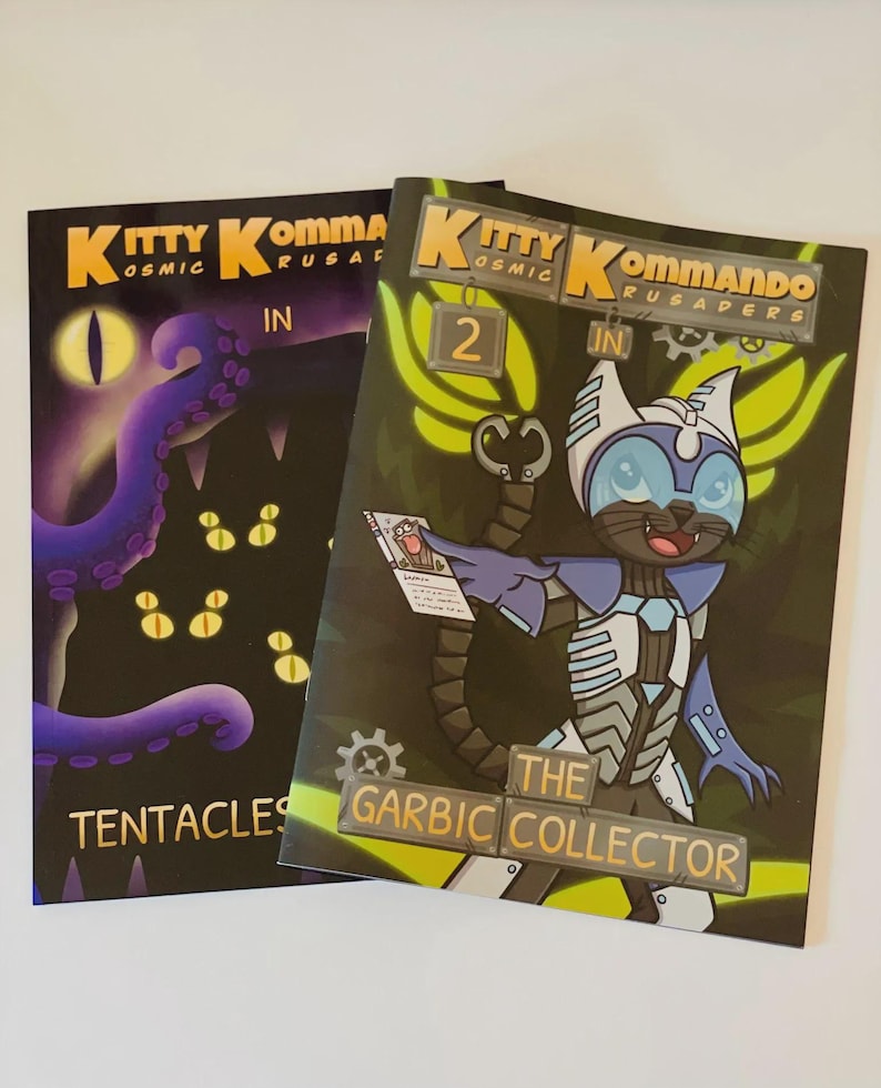 K&ouml;nnte beinhalten: Zwei Comic-Hefte mit dem Titel "Kitty Kommandos" werden gezeigt. Eines zeigt einen lila Oktopus und das Wort "Tentacles". Das andere zeigt eine Katze in einem Raumanzug mit dem Text "The Garbic Collector".