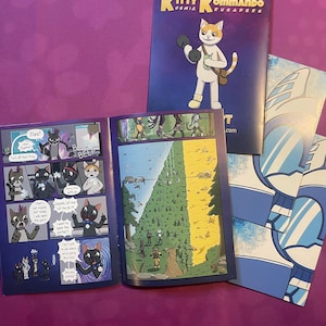 K&ouml;nnte beinhalten: Comic-Buch mit dem Titel "Kitty Kommando Cosmic Crusaders" mit einer Katzenfigur mit einer Hantel. Der Comic ist ge&ouml;ffnet, um Innenseiten mit Cartoon-Illustrationen zu zeigen. Zus&auml;tzliche Comic-Buchseiten sind sichtbar.