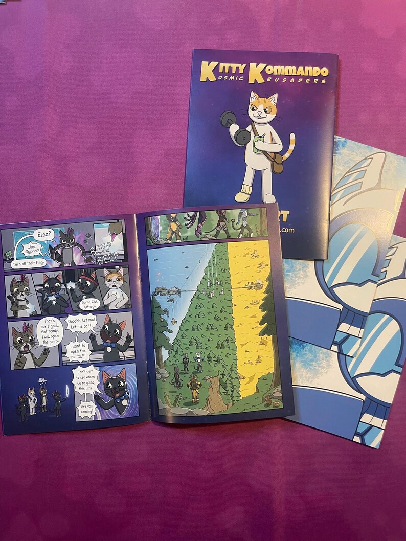 K&ouml;nnte beinhalten: Comic-Buch mit dem Titel "Kitty Kommando Cosmic Crusaders" mit einer Katzenfigur mit einer Hantel. Der Comic ist ge&ouml;ffnet, um Innenseiten mit Cartoon-Illustrationen zu zeigen. Zus&auml;tzliche Comic-Buchseiten sind sichtbar.