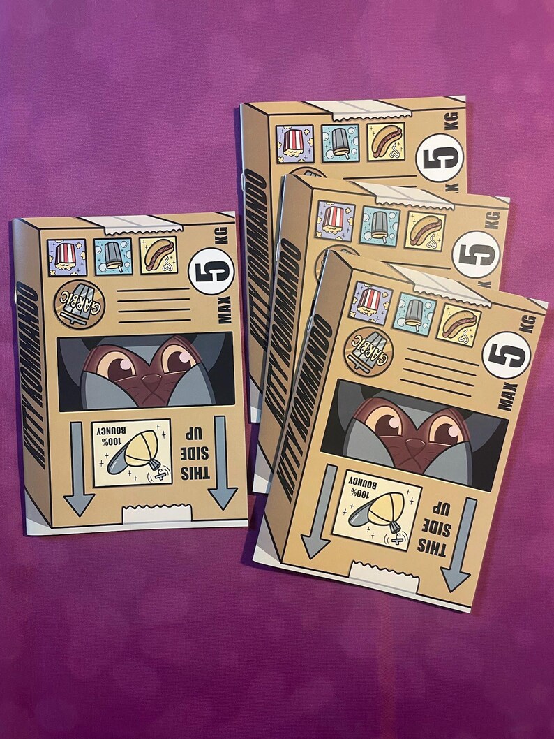 K&ouml;nnte beinhalten: Mehrere Pappkartons mit dem Text "KITTY KOMMANDO" und Illustrationen eines Katzenkopfes. Jede Box hat eine Gewichtsbeschr&auml;nkung von 5 kg. Die Boxen zeigen auch Essenssymbole und den Text "THIS SIDE UP".