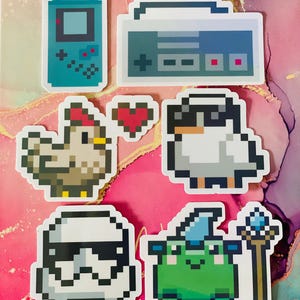 May include: A set of six pixel art stickers featuring a retro handheld game console, a boombox, a chicken with a red comb, a penguin wearing a black hat, a Stormtrooper, and a green frog wearing a blue wizard hat and holding a wand.