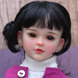 Peut inclure: Poupée aux cheveux noirs coiffés en chignon latéral et frange. La poupée a le teint clair, les joues roses et les lèvres pulpeuses. Elle porte un pull à col roulé blanc et une veste magenta à deux gros boutons.