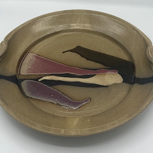 May include: A large, oval ceramic serving platter with two handles. The platter has a brown glaze with black and pink accents.
