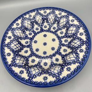May include: A white ceramic bowl with a blue and green lace pattern. The bowl has a scalloped edge and is perfect for serving soup or salad.