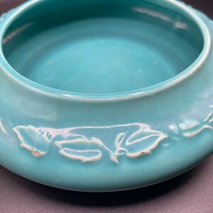 May include: A teal ceramic bowl with a decorative leaf design. The bowl is glazed and has a smooth, rounded shape.