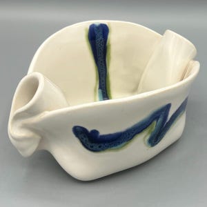 May include: White ceramic serving dish with a unique, folded design. The dish features blue and green abstract patterns.