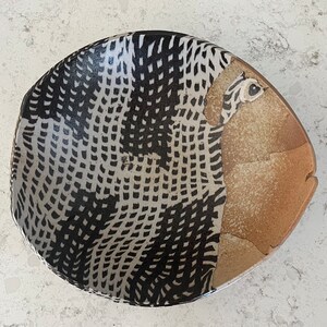 May include: A ceramic bowl with a black and white geometric pattern and a brown glaze on the rim.