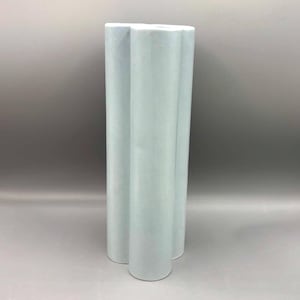 May include: A tall, light blue ceramic vase with a unique, fluted design. The vase has a rounded base and a series of vertical, curved sections that create a flower-like shape. The vase is a solid color and has a matte finish.