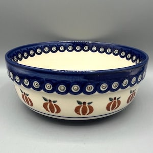 May include: A large, white ceramic bowl with a blue rim and a pattern of small blue circles. The bowl is decorated with a repeating pattern of orange pumpkins with green stems.