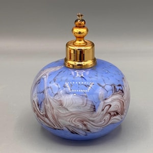 May include: A round, blue glass perfume bottle with a gold-colored metal top. The glass has a marbled pattern of white and brown swirls. The bottle is a decorative item.