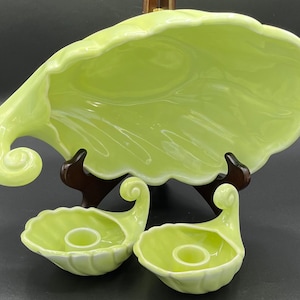 May include: A set of three vintage ceramic serving dishes in a pale green color. The large dish is shaped like a leaf and has a scalloped edge. The two smaller dishes are shaped like seashells and have a small indentation in the center for a candle.