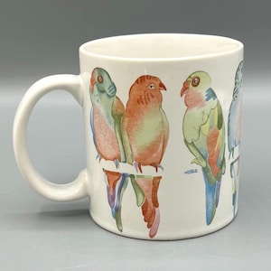May include: White ceramic mug with a colorful illustration of four parrots on a branch. The mug has a handle and the word "Noble" is printed on the bottom.