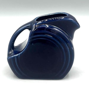 May include: A small, dark blue ceramic pitcher with a rounded shape and a single handle. The pitcher has a smooth, glossy finish.