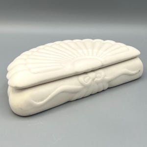 May include: A white ceramic trinket box shaped like a seashell with a fan-shaped design on the lid.