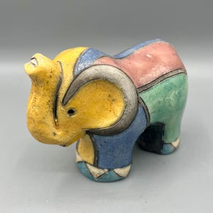 May include: A colorful ceramic elephant figurine. The elephant is segmented with yellow, blue, pink, and green sections. The ears and outlines are a metallic gray. The figurine has a textured surface and is a decorative item.