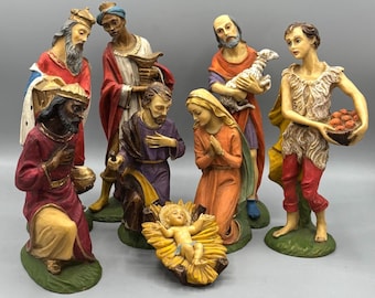 May include: A detailed nativity scene with multiple figurines. The figures include the three wise men, Mary, Joseph, a shepherd, and baby Jesus in a manger. The figurines are painted with vibrant colors and set on green bases.