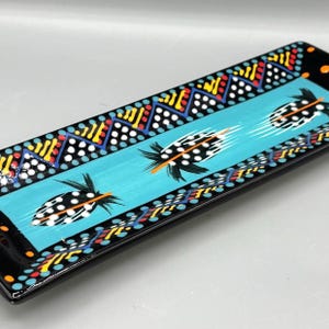 May include: A rectangular, hand-painted serving tray with a black border and a turquoise center. The tray features a feather design with black and white polka dots and orange accents. The border has a colorful geometric pattern.