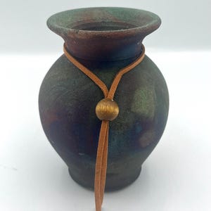 May include: A small, round, green, brown, and blue ceramic vase with a brown leather cord and a gold bead.