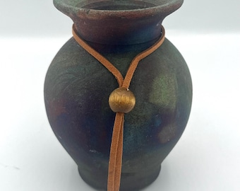 May include: A small, round, green, brown, and blue ceramic vase with a brown leather cord and a gold bead.