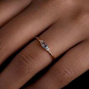 Peut inclure: Une délicate bague en or avec une pierre ovale bleu clair et de plus petites pierres claires de chaque côté.