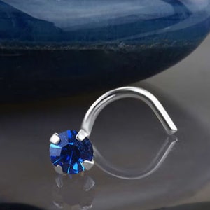 May include: A silver nose ring with a blue gemstone. The ring is curved and has a small, round stone in the center.