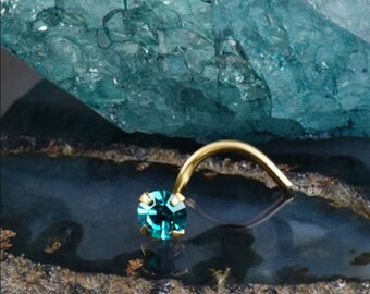 May include: A gold nose ring with a turquoise gemstone. The ring is curved and has a small, round stone.