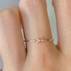 Peut inclure: Une délicate bague en or avec trois petites pierres précieuses claires. La pierre centrale est légèrement plus grande que les deux pierres de chaque côté.