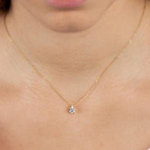 Puede incluir: Un delicado collar de oro con un pequeño colgante de diamante en forma de pera. El colgante está engastado con múltiples facetas, reflejando la luz. El collar se lleva en el cuello de una persona, mostrando la sutil elegancia de la joya.