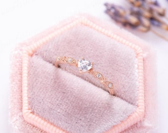 May include: A delicate rose gold ring with a small heart-shaped clear stone and smaller clear stones set in a band.