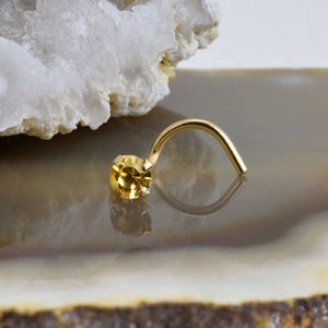 May include: A gold nose ring with a small, round, yellow gemstone.