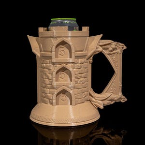 May include: A beige 3D printed mug shaped like a stone tower with a dragon handle. The mug has three arched openings on the front, each with the number "5" inside. A black can with green text is sitting on top of the tower.