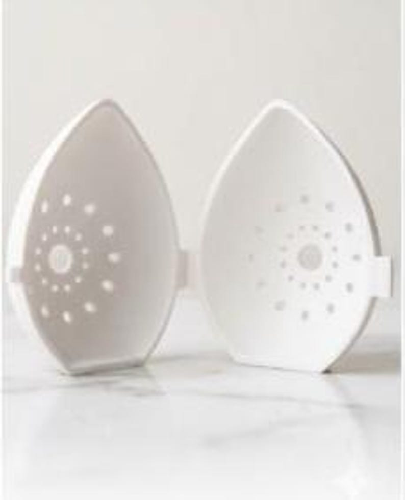 May include: Two white, teardrop-shaped, microwave egg cookers, open to reveal the interior. Each half has a series of small, circular holes arranged in a spiral pattern. The cookers are designed to cook eggs in the microwave.